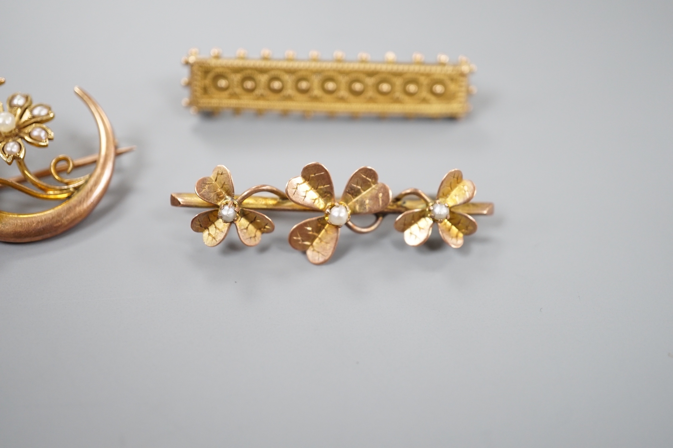 A late Victorian 15ct and seed pearl set flower and crescent brooch, 22mm, gross 3.1 grams and two later yellow metal bar brooches, gross 6 grams.